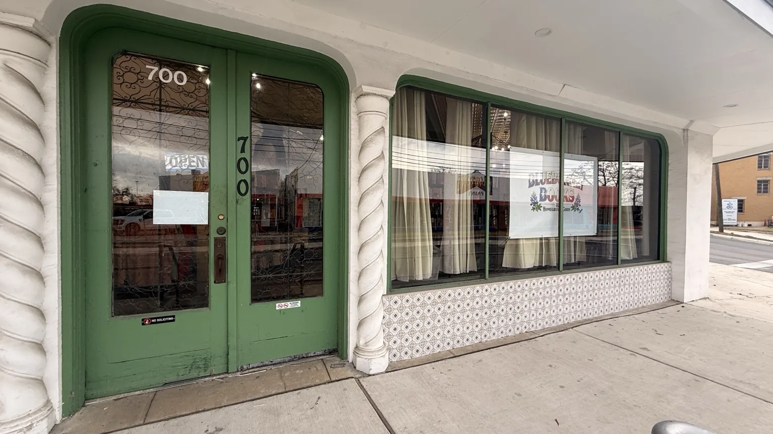 Front entrance of Bluebonnet Books & Homegrown Goods with green-trimmed doorway and street-facing windows.