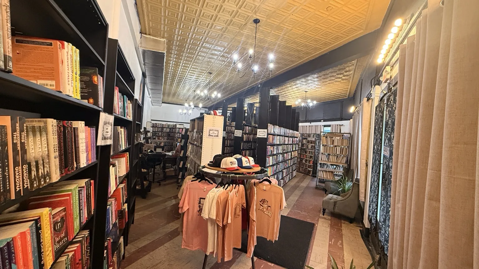 Interior view of the bookstore with tall shelves, merchandise, and a patterned ceiling.