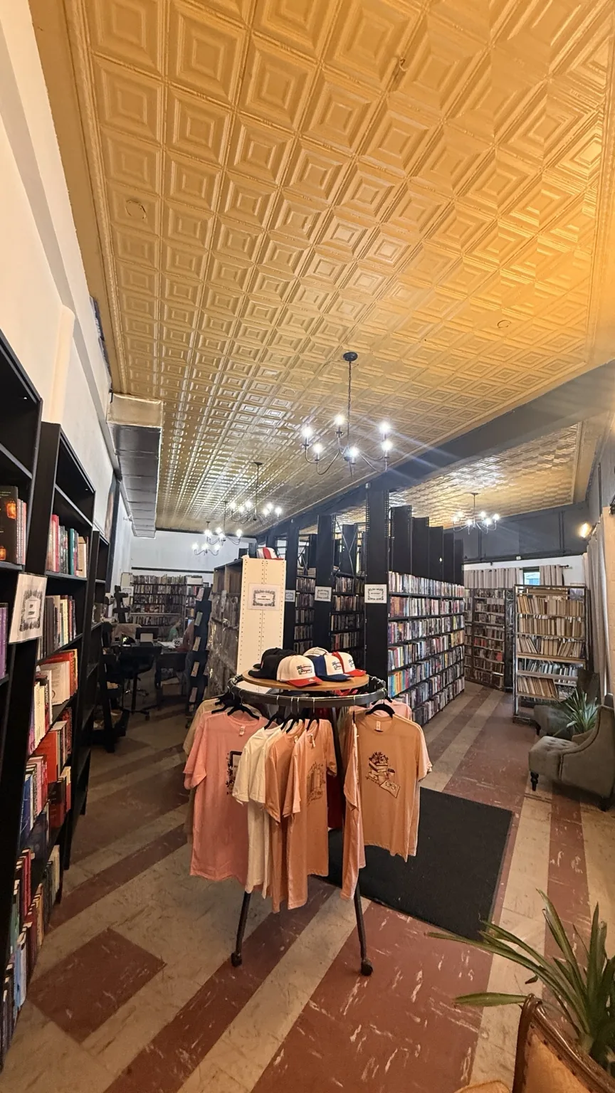 Vertical interior photo showing the patterned ceiling, bookshelves, and merchandise display.